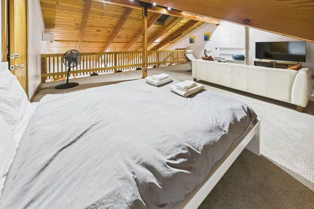 Un dormitorio con una cama grande, un sofá blanco, un televisor y un techo de madera.