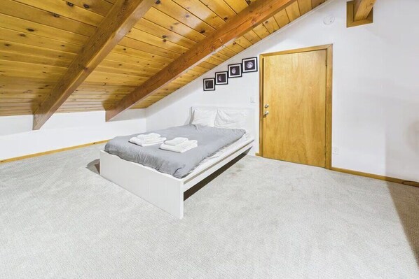 A bedroom with a bed, a wooden door, and a sloped ceiling.