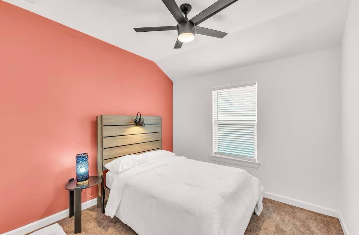 A bedroom with a bed, a ceiling fan, a nightstand, and a window with blinds.