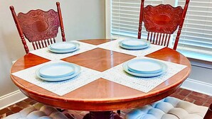 Une table de salle à manger ronde en bois, accompagnée de quatre chaises, chacune dotée d’un siège rembourré. La table est mise avec des assiettes blanches et des serviettes bleues.