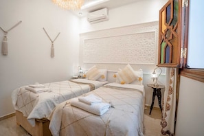 A hotel room with two beds, a decorative wall, a small table with a lamp, and a hanging light fixture. - Dar Mawati (Marrakech)