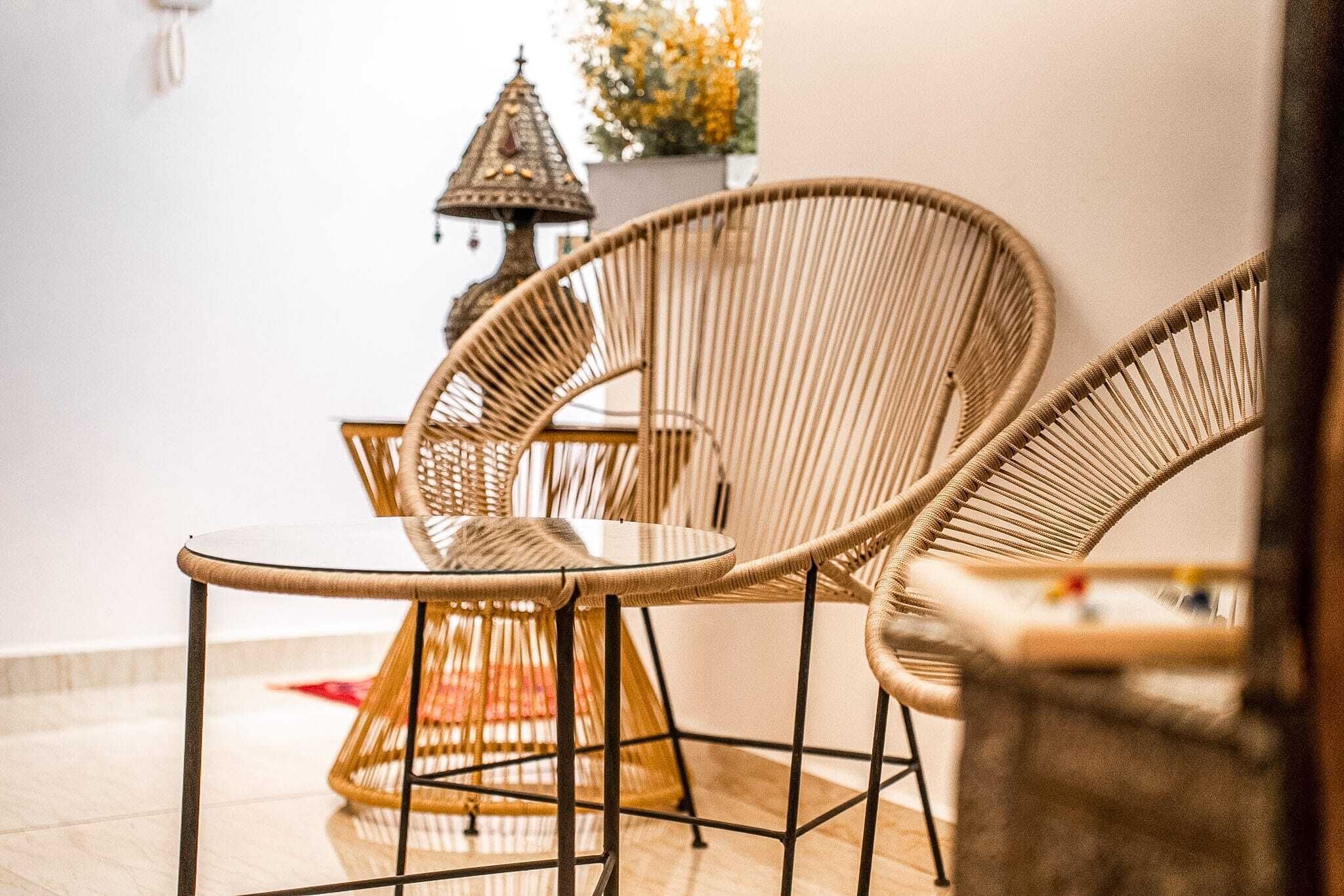 A room with wicker chairs and a glass table, a decorative lantern, and a potted plant.