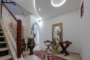 Un escalier avec une rampe blanche, un tapis à motifs et un miroir avec un cadre doré.