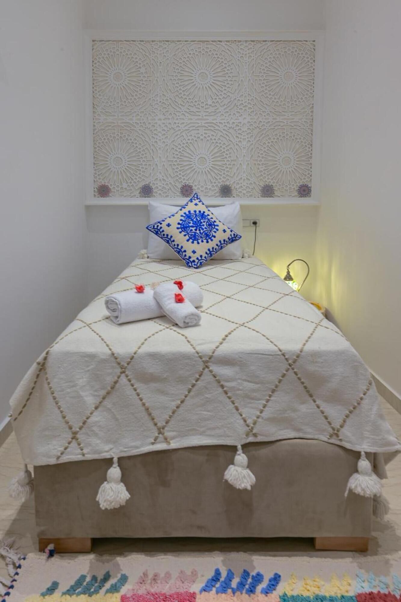 A neatly made bed with a patterned bedspread, a decorative pillow, and rolled towels.