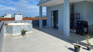 Terraza en la azotea con jacuzzi, plantas en macetas y una parrilla.