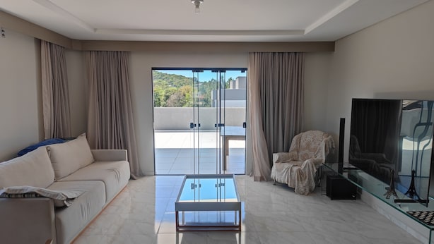 Una sala de estar moderna con sofá, sillón, mesa de centro de vidrio y televisor sobre un mueble.