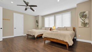 Quarto com duas camas, ventilador de teto e janela com persianas.