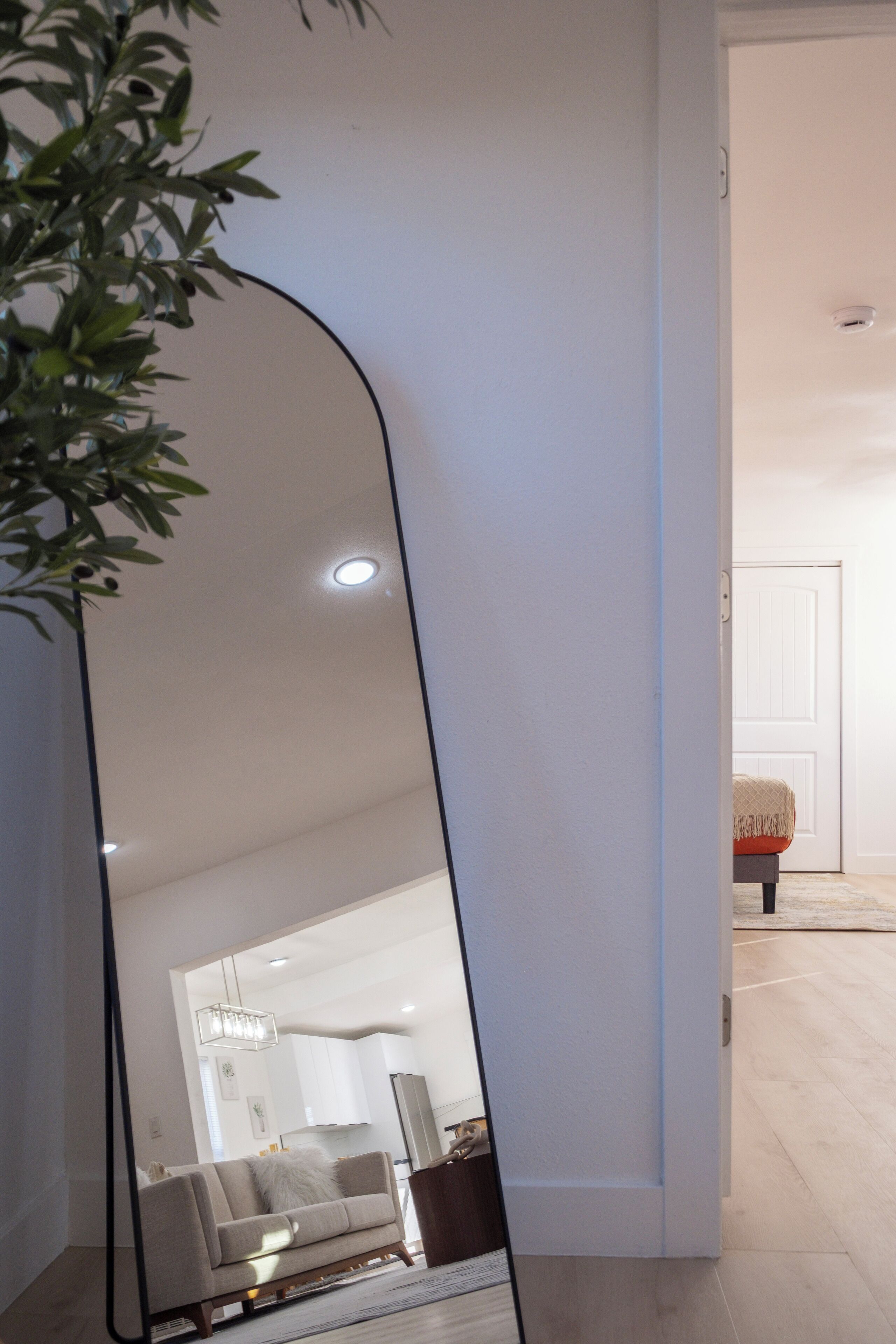 A modern living room with a large mirror reflecting the space, a sofa, and a dining area in the background.