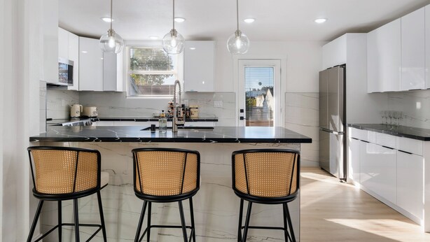 A modern kitchen with a marble island, three bar stools, stainless steel appliances, and pendant lighting. - Modern Seattle Retreat 4BR Home Near Downtown (Seattle)