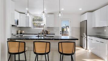 A modern kitchen with a marble island, three bar stools, stainless steel appliances, and pendant lighting.