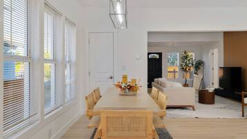A modern living room with a large TV, a sofa, and a dining area with a table and chairs.