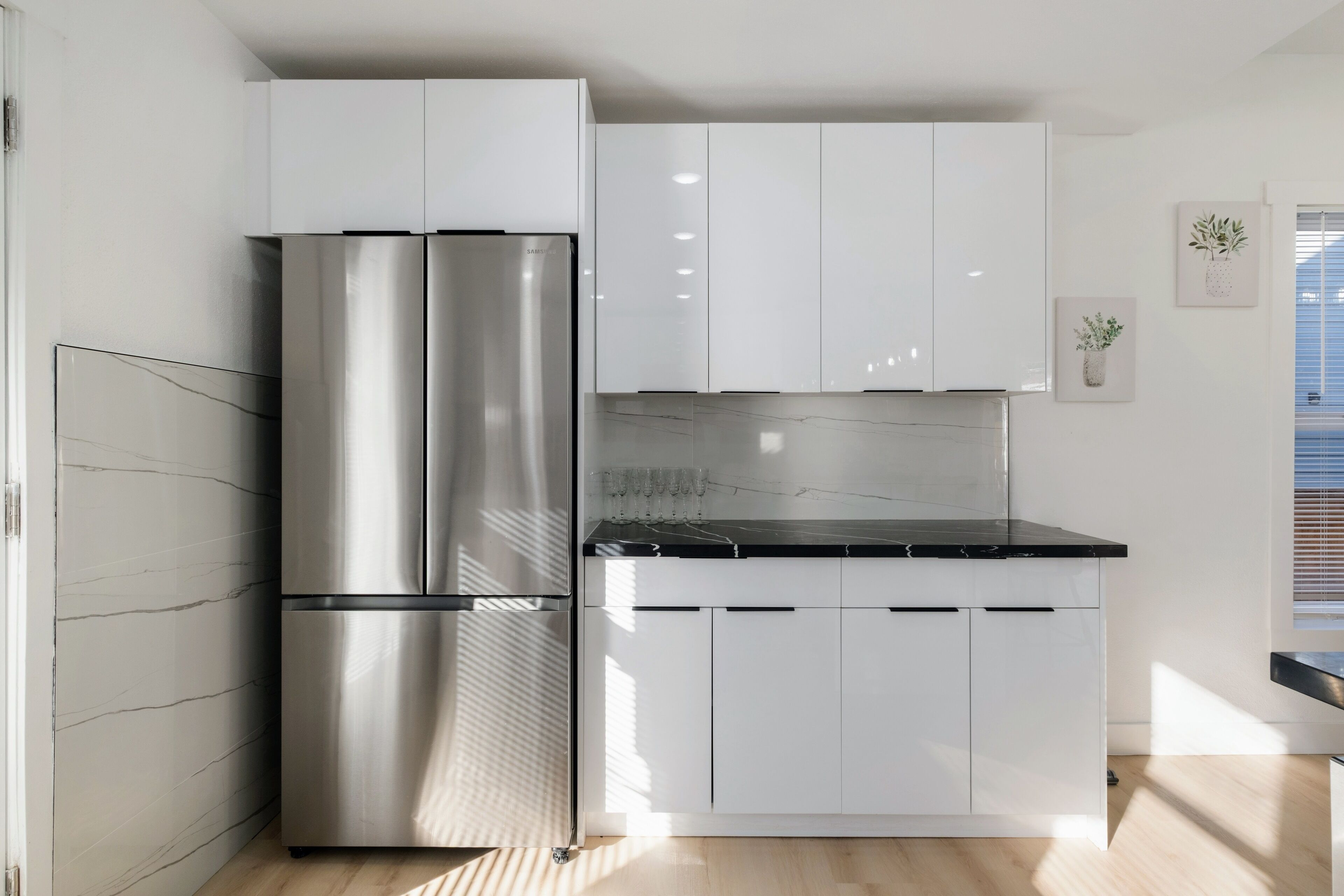Una cocina moderna con armarios blancos, un refrigerador de acero inoxidable y una encimera negra.