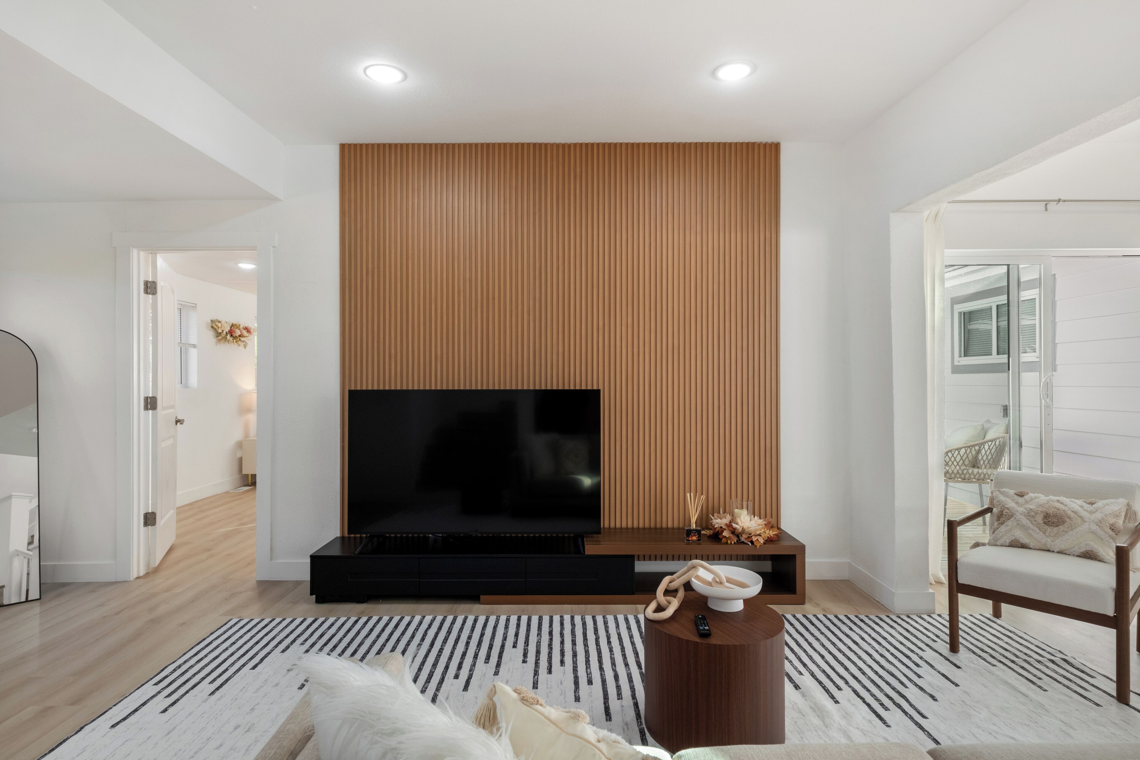 A modern living room with a large flat-screen TV, wooden panel wall, and a comfortable seating area with a sofa and armchair.