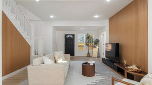 A modern living room with a sofa, coffee table, and TV. A staircase is visible on the left, and a wooden panel wall is on the right. - Modern Seattle Retreat 4BR Home Near Downtown (Seattle)