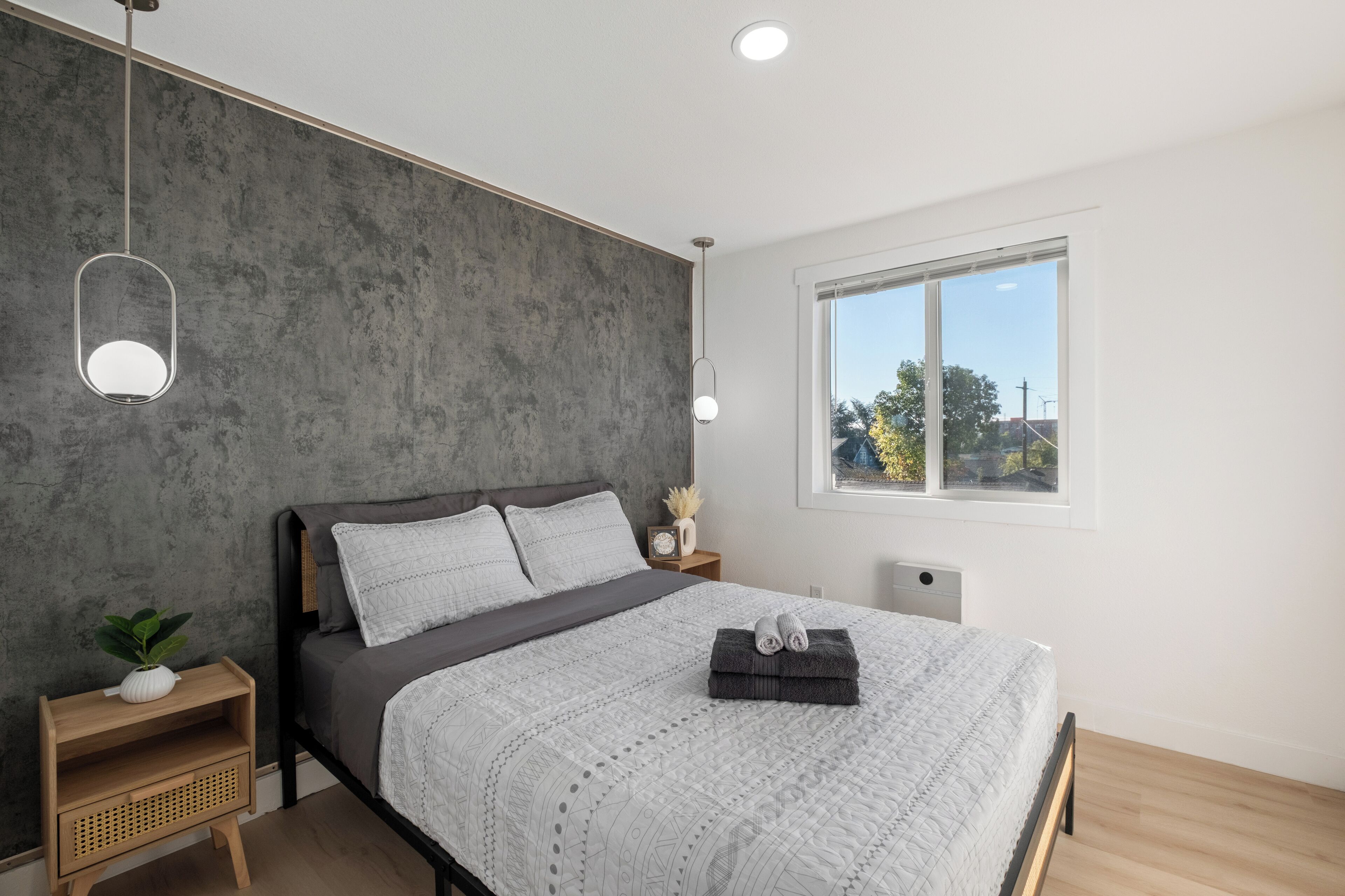 Une chambre moderne avec un grand lit, une table de chevet agrémentée d’une plante, une fenêtre offrant une belle vue et un mur au revêtement original.
