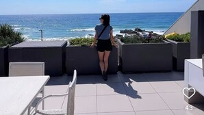 A woman standing on a patio overlooking the ocean.