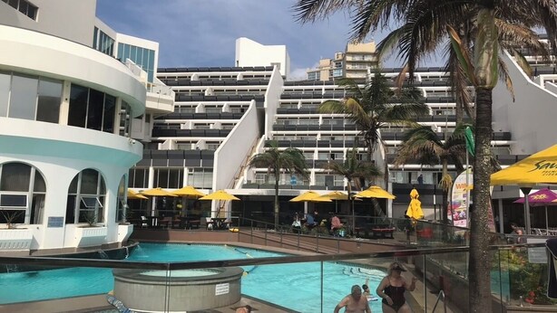 A hotel pool area with multiple swimming pools, palm trees, and outdoor seating with umbrellas.