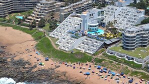 A coastal hotel with multiple buildings, a beach, and a pool area.