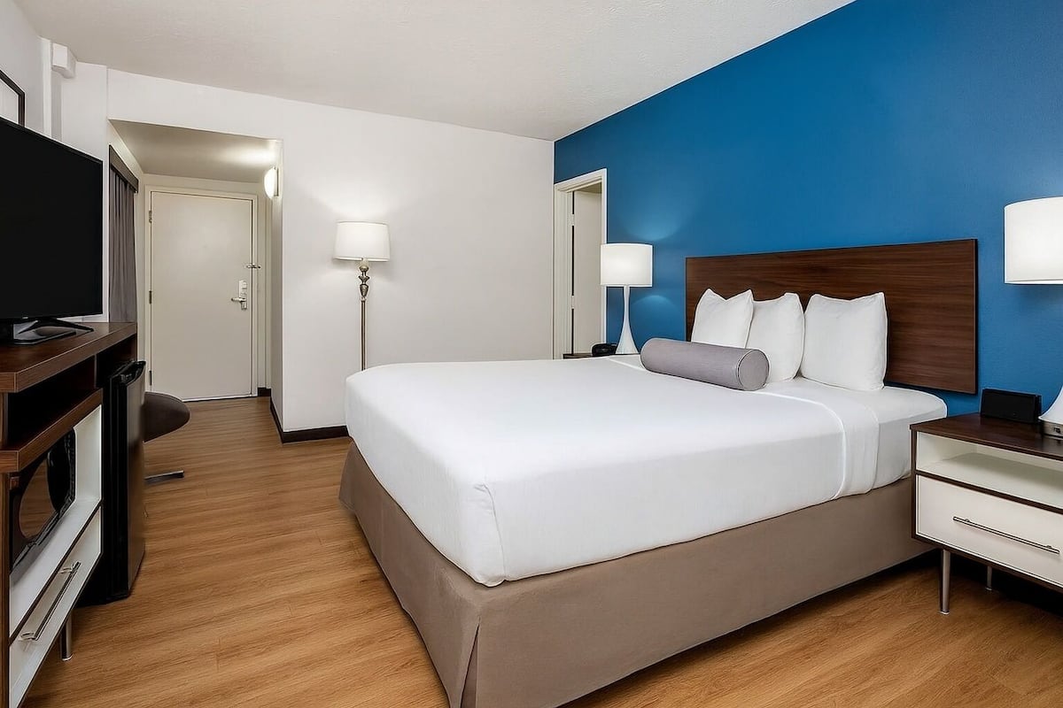 Una habitación de hotel con una cama grande, mesitas de noche, televisión y escritorio.