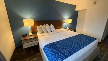 Habitación de hotel con cama, dos lámparas de noche, una mesita de noche y un reloj digital.