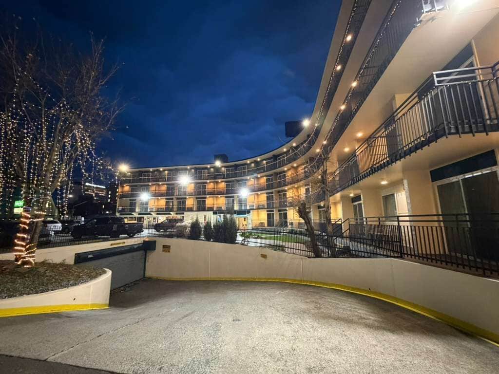 Um hotel de vários andares com fachada curva, estacionamento externo e uma árvore decorada com luzes.
