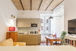 Un ambiente compatto con angolo cottura, zona pranzo e televisione.
