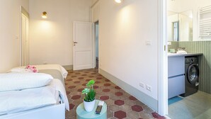Habitación de hotel con una cama, una mesita con una planta y un control remoto, una lavadora y un espejo.