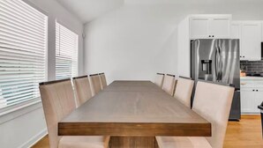 A modern kitchen with white cabinets, a stainless steel refrigerator, and a wooden dining table with six chairs. - HTX NRG + Med Center (Houston)
