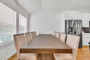 Eine moderne Küche mit weißen Schränken, einem Edelstahl-Kühlschrank und einem Holztisch mit sechs Stühlen.