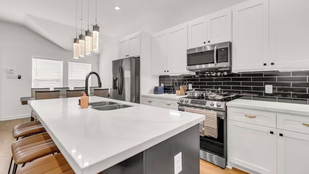 A modern kitchen with white cabinets, a stainless steel refrigerator, a microwave, and a gas stove. - HTX NRG + Med Center (Houston)