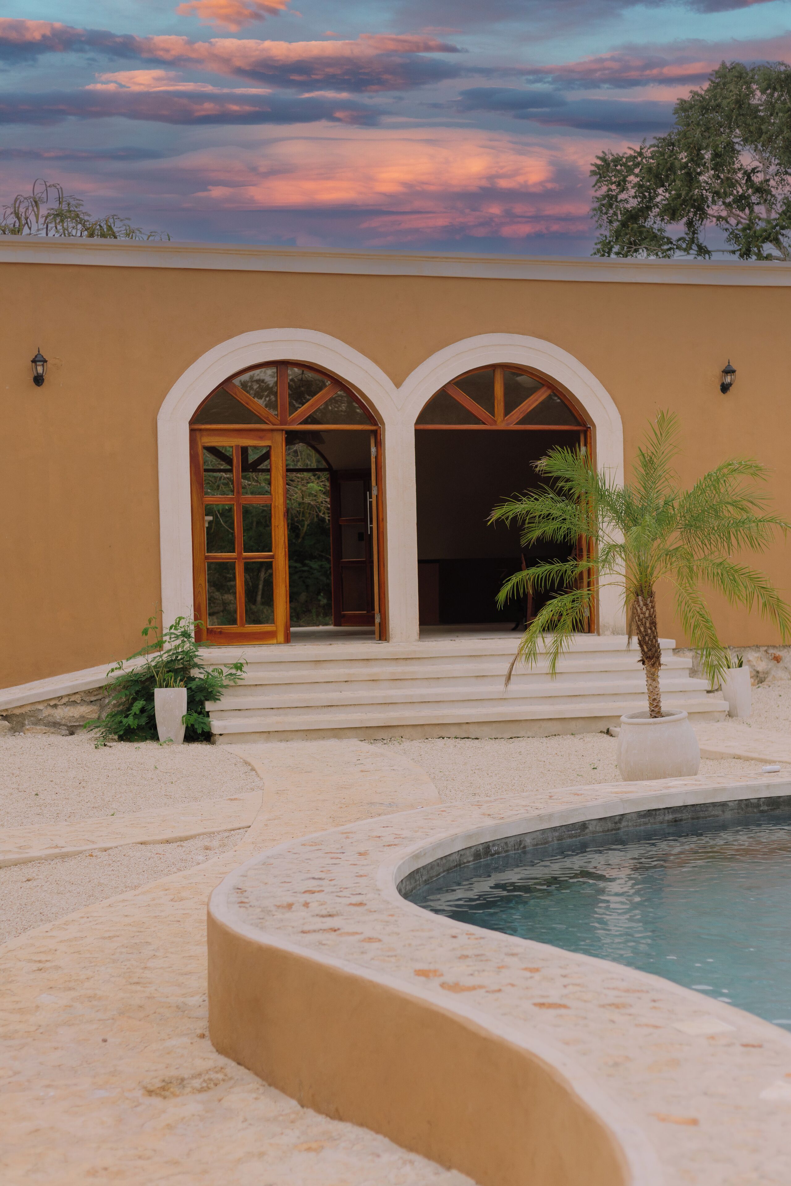A building with two arched doorways, a pool, and a palm tree.