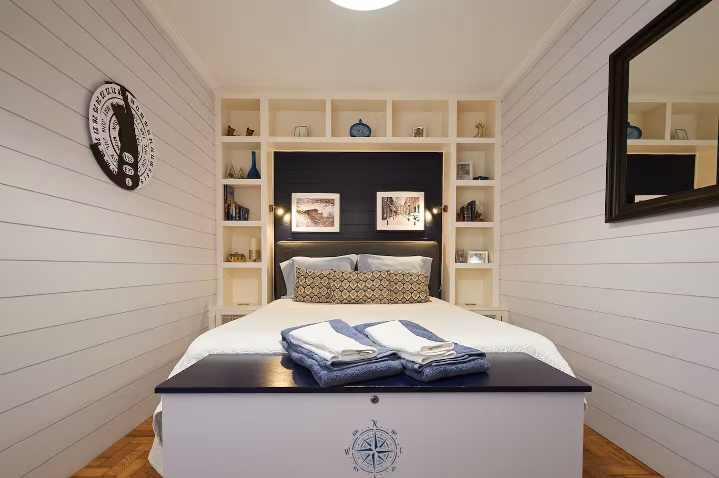 A neatly arranged bedroom with a bed, bedside tables, a wall clock, and a mirror.
