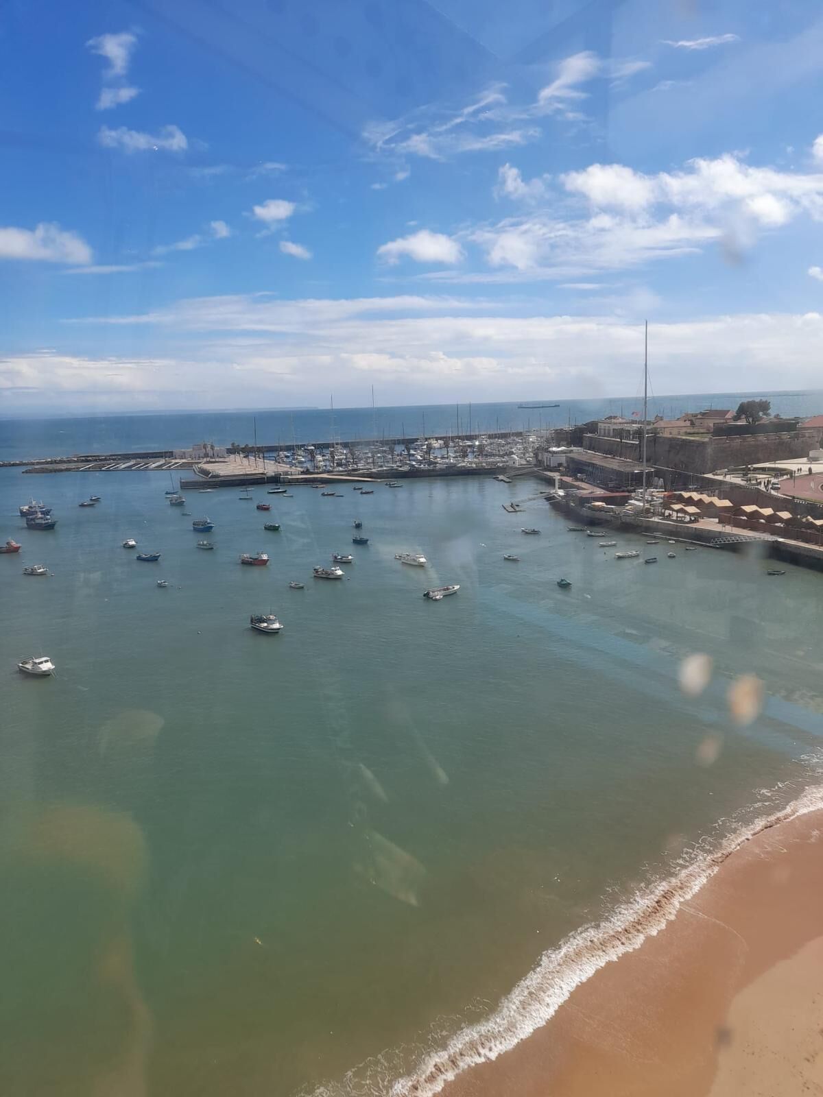 Eine Küstenstadt mit einem Hafen voller Boote, einem Sandstrand und einer befestigten Struktur im Hintergrund.