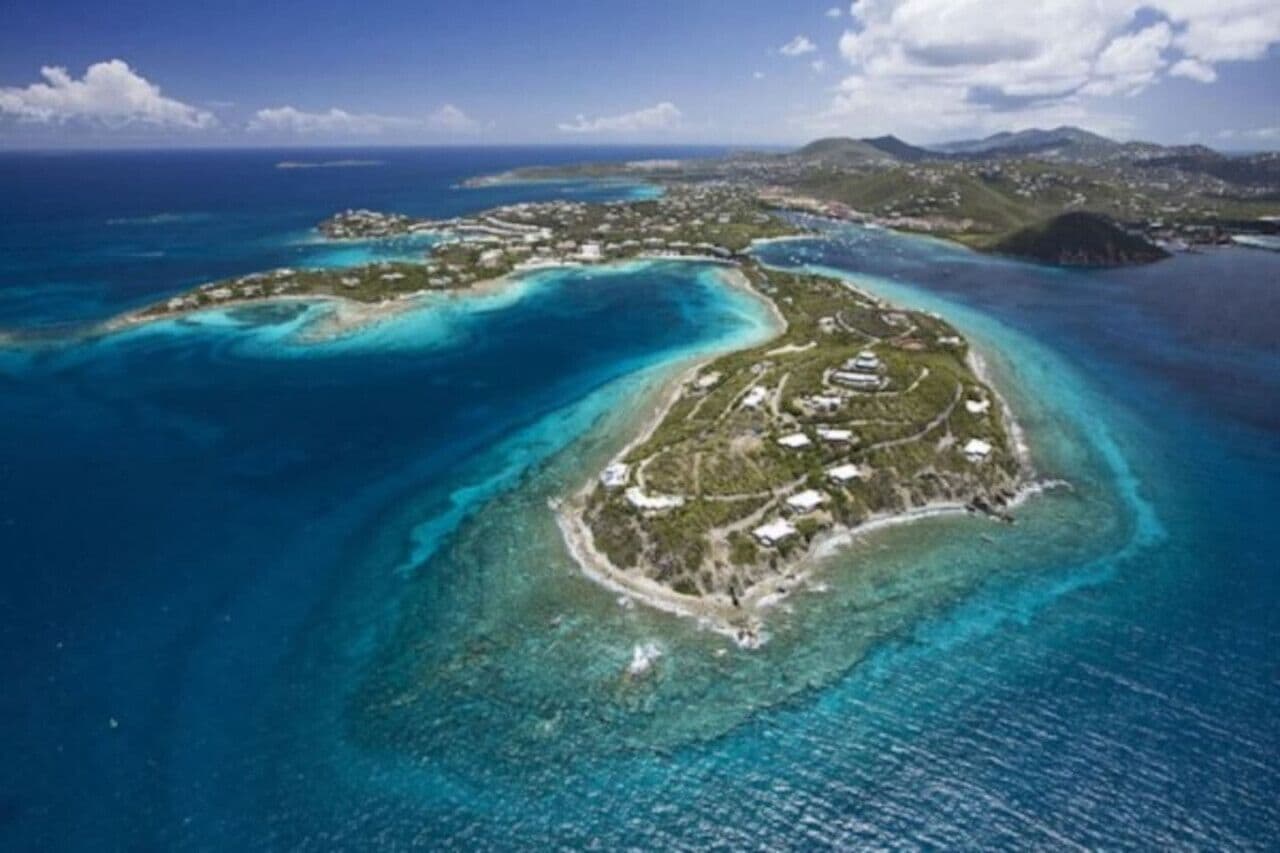 An aerial view of a coastal island with clear blue waters and a small settlement.