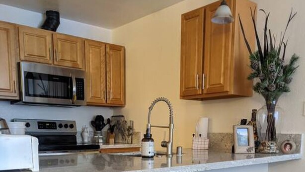 A kitchen with wooden cabinets, a stainless steel microwave, a gas stove, a sink, and four bar stools with twisted legs.