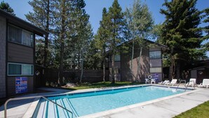 A rectangular swimming pool with a metal ladder, surrounded by a concrete deck. There are white lounge chairs and a small grassy area.