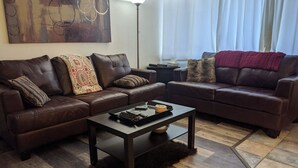 A modern living room with two brown leather sofas, a dark wooden coffee table, and a patterned throw pillow.