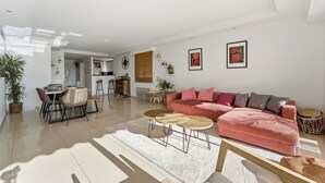A spacious living room with a large sofa, a dining area, and a kitchen in the background. - Appartement Margot - Welkeys (Le Cannet)