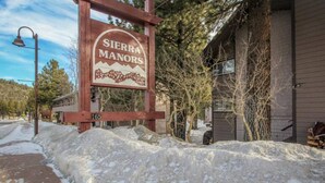 Une enseigne indiquant « Sierra Manors », un bâtiment à l’aspect rustique, avec le numéro « 165 » bien visible et de la neige au sol.