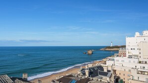 A coastal town with buildings near the beach and a lighthouse in the distance. - Appartement Okéana - 3 étoiles - Welkeys (Biarritz)