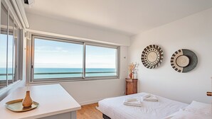 A bedroom with a large window, a bed, a bedside table, and two wall-mounted decorative plates. - Appartement Okéana - 3 étoiles - Welkeys (Biarritz)