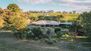 A house with a solar panel roof, surrounded by a lush landscape and a vineyard in the background. - Vineyard Retreat in the Heart of McLaren Vale (McLaren Vale)