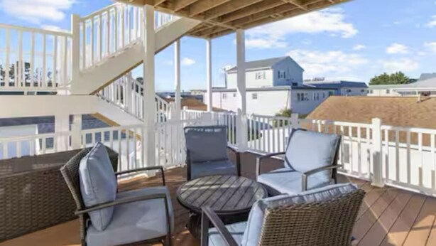 A covered outdoor deck with wicker furniture, a staircase, and a white fence. - Bayside Park Villa at Robin Drive (Ocean City)