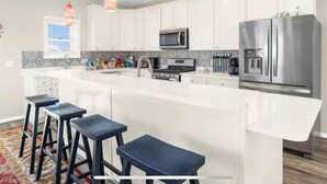 A modern kitchen with white cabinets, stainless steel appliances, and a central island with bar stools. - Bayside Park Villa at Robin Drive (Ocean City)
