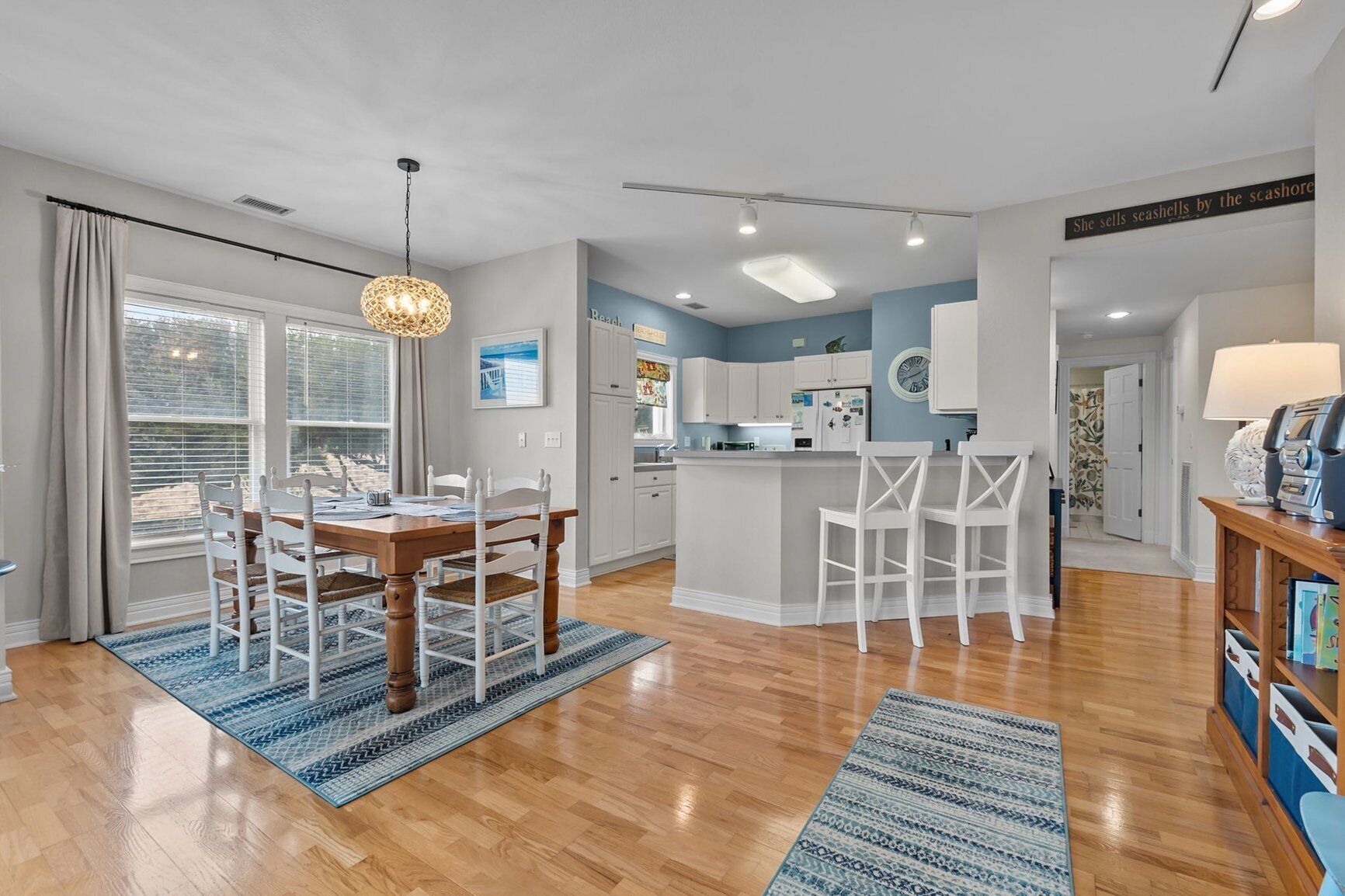 A modern kitchen with white cabinets, a central island, and a dining area with a wooden table and white chairs.