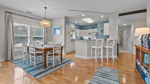 Une cuisine moderne avec des meubles blancs, un îlot central et un coin repas comprenant une table en bois et des chaises blanches.