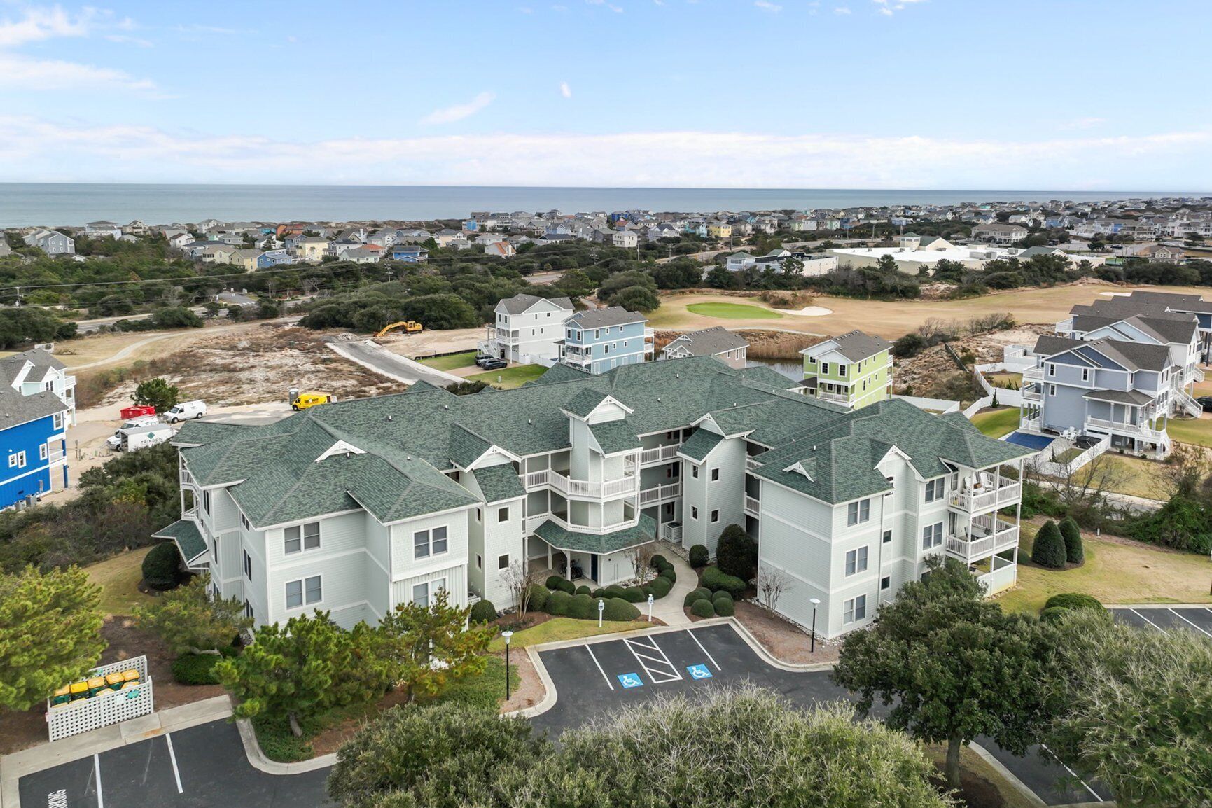A multi-story residential building with a green roof, surrounded by a parking lot and greenery.