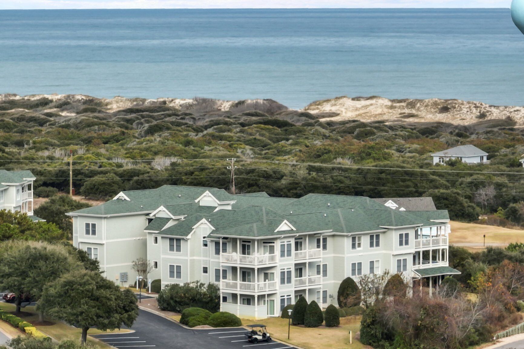 A multi-story building with a green roof, located near a beach with dunes and vegetation.