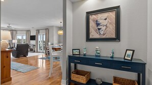 Un salon moderne avec un plancher en bois, une console bleu foncé agrémentée d’objets décoratifs, une grande peinture abstraite et une vue sur la salle à manger.