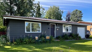 A small, single-story house with a dark exterior, numbered 3636, featuring a front door, two windows, and a garage door. - Cozy 3-bedroom house in Anchorage (Anchorage)